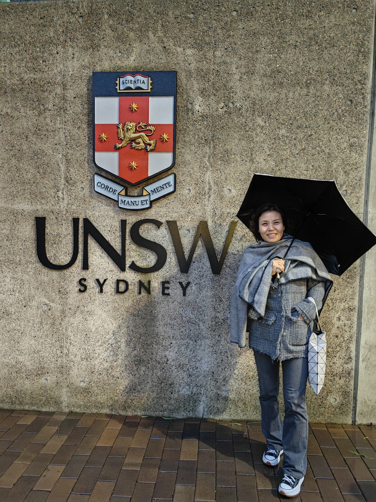 撑伞的人站在 UNSW 校徽旁